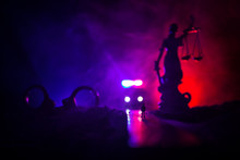 Legal Law Concept. Silhouette Of Handcuffs With The Statue Of Justice On Backside With The Flashing Red And Blue Police Lights At Foggy Background. Selective Focus