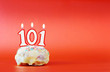 One hundred and one years birthday. Cupcake with white burning candle in the form of number 101. Vivid red background with copy space