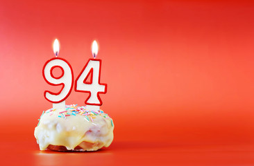 Ninety four years birthday. Cupcake with white burning candle in the form of number 94. Vivid red background with copy space