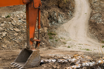 Excavator bucket on the background of a stone quarry, quarry road and fallen tree trunks