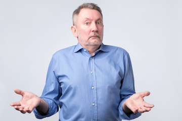 Wall Mural - Confused senior caucasian man in blue shirt is unsure in studio