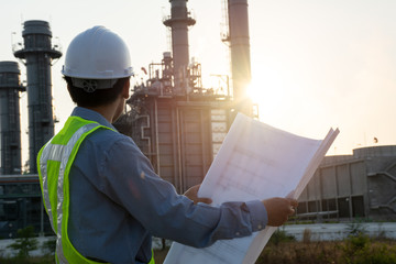 Engineers male are looking at blueprint for workers security control at power plant. Energy power station area with sky, sunset. Concept safety,industry