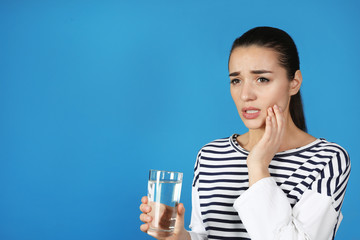 Wall Mural - Emotional young woman with sensitive teeth and glass of water on color background. Space for text