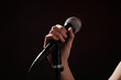 © New Africa - Woman holding microphone on black background, closeup