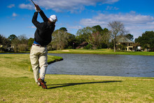 Amateur Golfer In Action Shot Hitting With Ball Heading Towards The Pin Hole Over Water