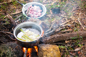 Ingredient of soup in boil water in a pot on campfire.