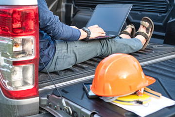 Young Asian field worker with tools sitting on pickup trunk. Working in field.