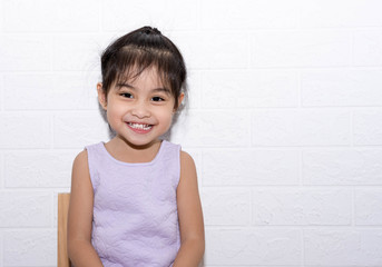 Female asian child girl sitting on a chair with white background smiling