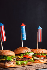 Wall Mural - three fresh and juicy burgers with American flag-style fireworks inserted into them. bbq concept picnic to celebrate independence day