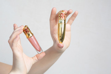 Poster - Female hand holding lip gloss and lipstick in a designer packaging over a grey background. Empty space