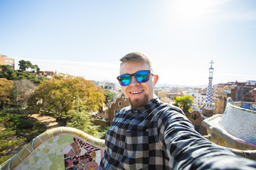 Wall Mural - Travel and holidays concept - Happy guy making selfie portrait with smartphone in Park Guell, Barcelona, Spain.