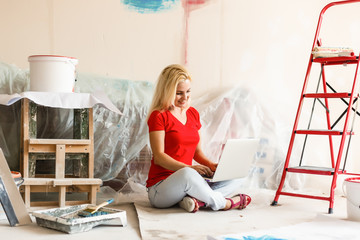 Wall Mural - Young woman portrait while painting new apartment ,sitting with laptop. Young woman with laptop