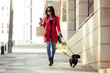© nenetus - Stylish young woman walking with her little dog while texting with her smartphone on the street in the city.