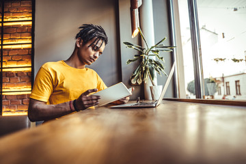 Stylish student with African hairstyle wearing casual clothes having doubtful look while looking at laptop computer not understanding new material trying to find good explanation in internet.