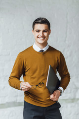 Wall Mural - Smilling  handsome  businessman in yellow sweater, hand hold gray laptop at his office.