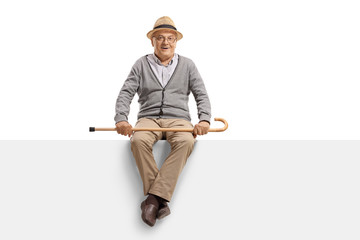 Wall Mural - Senior man sitting on a blank billboard panel and holding a walking cane