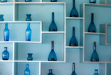 Blue Glass Bottles On Shelves Attached To A Light Blue Wall.