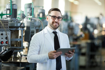 Waist up portrait of handsome factory worker holding digital tablet posing  in workshop and smiling at camera, copy space