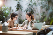 © Seventyfour - Jolly confident enterprising ladies in casual shirts sitting at table in modern cafe and viewing papers while working on report