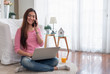 © weedezign - Happy asian woman talk on mobile and  typing laptop computer at home.female freelancer sitting on carpet on floor work at home in living room