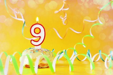 Nine years birthday. Cupcake with burning candle in the form of number 9. Bright yellow background with copy space