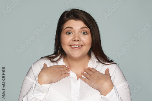 You mean me? Fascinated amazed young plus size woman in white shirt pointing at herself, holding hands on her chest and smiling broadly as being chosen for job positive among other candidates