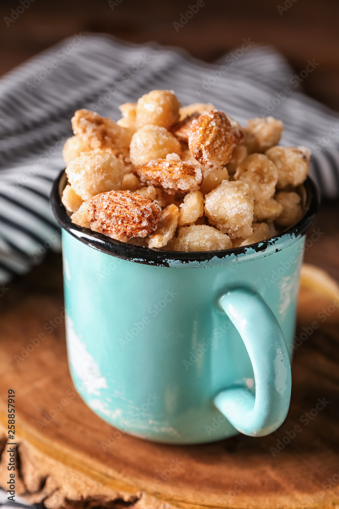 Cup with tasty sugared nuts on wooden board, closeup