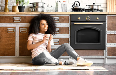 Wall Mural - African-American woman drinking coffee in kitchen