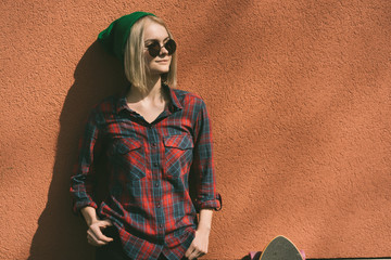 Fashionable blonde girl stands near the pink wall in the street on a sunny day