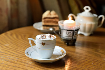 Coffee on cafe table with cake and candle in background