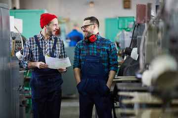 Portrait of two factory workers chatting and smiling standing in industrial workshop, copy space