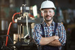 Waist up portrait of mature factory worker wearing hardhat looking at camera while standing in workshop, copy space