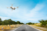 Fototapeta  - White drone with camera flying above the street with trees and grass