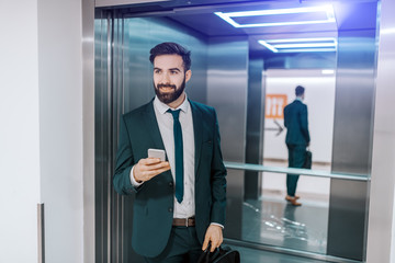 smiling caucasian businessman in formal wear holding briefcase and smart phone while getting out of 