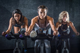 Group of young sporty women riding cycling bikes during spinning class indoors
