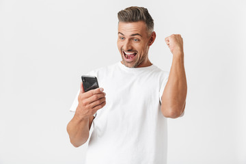 brunette man 30s wearing casual t-shirt rejoicing while using smartphone