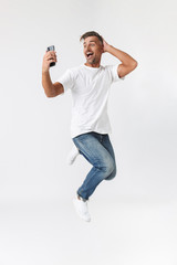 Poster - Full length image of cheerful man 30s wearing casual t-shirt holding and using mobile phone