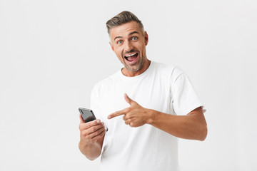 Wall Mural - Image of optimistic man 30s wearing casual t-shirt rejoicing while using smartphone