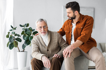 Wall Mural - happy senior father in glasses sitting near handsome son at home