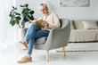 © LIGHTFIELD STUDIOS - senior man in glasses reading book while sitting in armchair at home