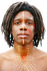 Portrait of young african man with dreadlocks and traditional face paint looking straight into the camera with a serious expression