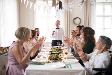 Wall Mural - A big family sitting at a table on a indoor birthday party, a senior man giving a speech.