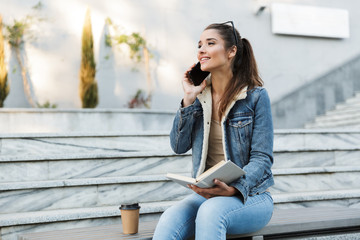 Canvas Print - Smiling young woman wearing jacket sitting on a bench