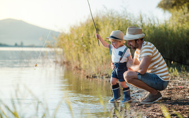 A mature father with a small toddler son outdoors fishing by a lake.