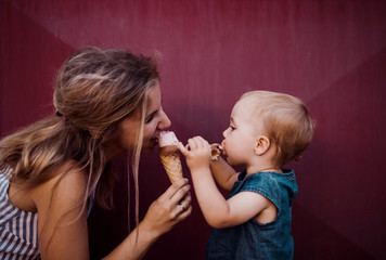 young mother with small toddler girl outdoors in summer, eating ice cream.