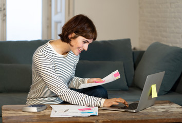 Portrait happy young woman sitting on the sofa surrounded by papers calculating and paying bills