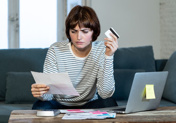 Stressed and overwhelmed young woman paying credit card debts and bills on laptop