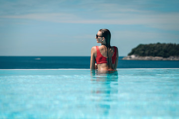 Young woman relaxaing in the swimming pool looking at the ocean view in background l. Beautiful seascape. Trip to warm destination. Phuket. Thailand.