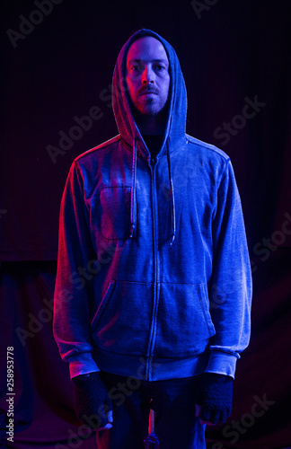 Cuadros en Lienzo A male model with stubble wearing a hood up in a dark atmospheric future colour setting