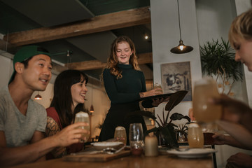 Wall Mural - Smiling watiress bringing customers drinks in a bar